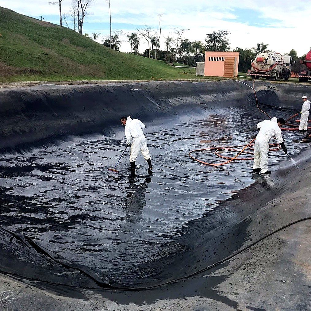 Operadores com macacão de proteção lavando o fundo de uma lagoa de tratamento com manta